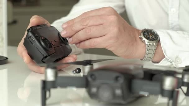 Hombre maduro con gafas y camisa blanca monta un panel de control para un quadrocopter, un concepto para el estudio de la tecnología, primer plano de una mano — Vídeos de Stock