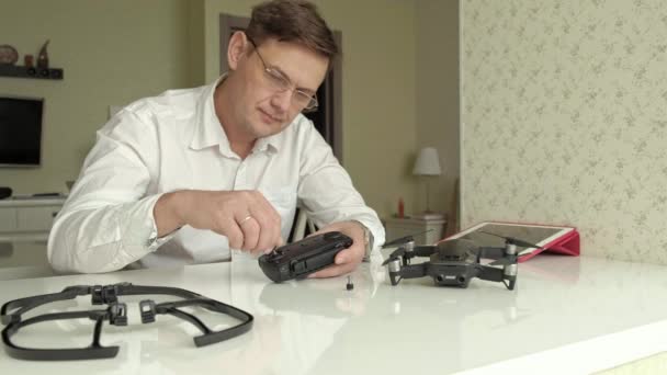 Mogen man med glasögon och en vit skjorta monterar en kontrollpanel för en quadrocopter, ett koncept för studiet av teknik — Stockvideo
