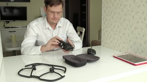 Homem maduro em óculos e uma camisa branca recolhe um quadricóptero, apresenta uma pá, conceito de estudar tecnologia — Vídeo de Stock