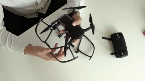 Reifer Mann mit Brille und weißem Hemd montiert einen Quadrocopter, installiert Schutz auf den Klingen, das Konzept des Technikstudiums, Draufsicht — Stockvideo