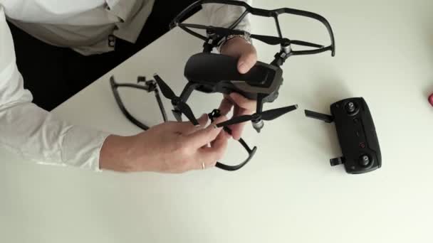 Homme mûr avec des lunettes et une chemise blanche assemble un quadrocopter, installe la protection sur les lames, le concept d'étude de la technologie, vue de dessus — Video
