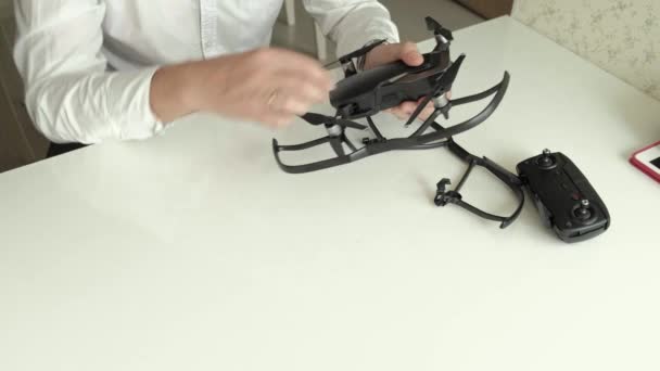 Mogen man med glasögon och en vit skjorta monterar en quadrocopter, installerar skydd på bladen, begreppet studerar teknik, ovanifrån — Stockvideo