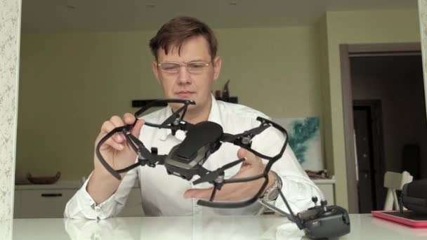 Homem maduro com óculos e uma camisa branca recolhe um quadricóptero, examina-lo, o conceito de estudar tecnologia — Vídeo de Stock