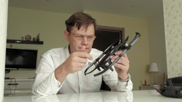 Reifer Mann mit Brille und weißem Hemd sammelt einen Quadrocopter ein, untersucht ihn, das Konzept des Technikstudiums — Stockvideo