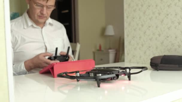 Зрелый мужчина в очках и белой рубашке управляет quadcopter из консоли, испытательный полет, концепция изучения технологии — стоковое видео