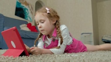 Pembe elbiseli sarışın saçlı küçük bir kız yerde yatıyor ve bir kalem tablet, boya resimler, 4 k bir portre çizer