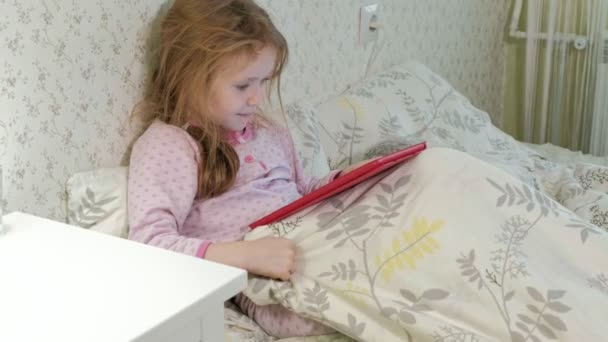 Kleines Mädchen spielt im Bett auf Tablet — Stockvideo