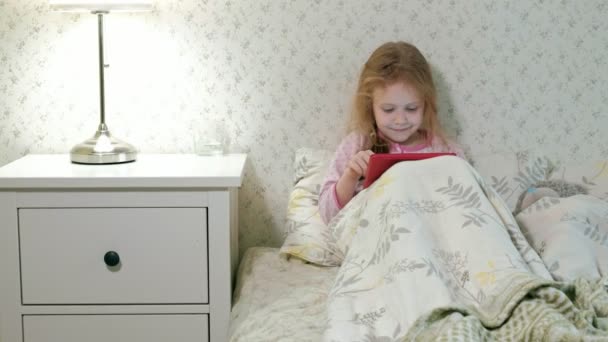 Niña en la cama jugando en la tableta — Vídeo de stock