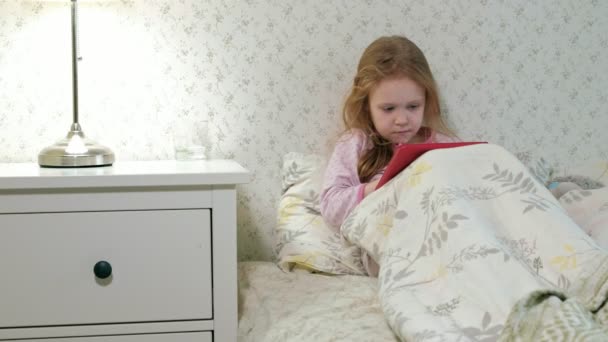 Niña en la cama jugando en la tableta — Vídeos de Stock