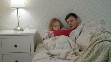 Baba ve küçük kızı tablet üzerinde oynarken yatakta