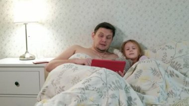 Baba ve küçük kızı tablet üzerinde oynarken yatakta