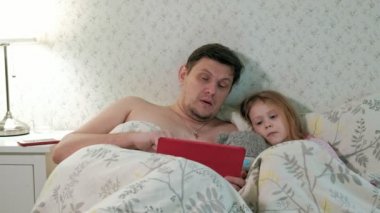 Baba ve küçük kızı tablet üzerinde oynarken yatakta