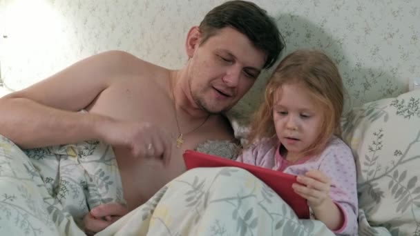Dad and little daughter on the bed playing on the tablet — Stock Video