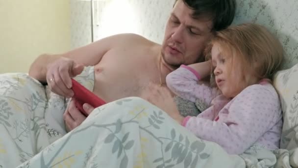Papa en dochtertje op het bed op de tablet spelen — Stockvideo