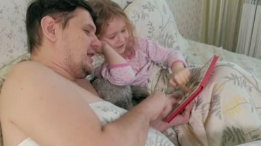 Baba ve küçük kızı tablet üzerinde oynarken yatakta