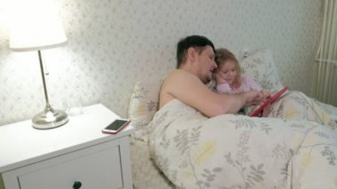 Baba ve küçük kızı tablet üzerinde oynarken yatakta