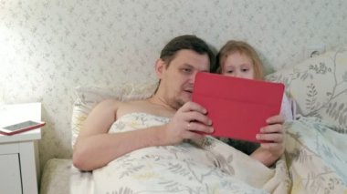 Baba ve küçük kızı tablet üzerinde oynarken yatakta