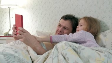 Baba ve küçük kızı tablet üzerinde oynarken yatakta