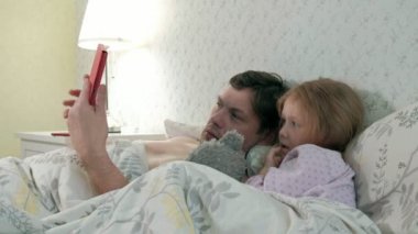 Baba ve küçük kızı tablet üzerinde oynarken yatakta