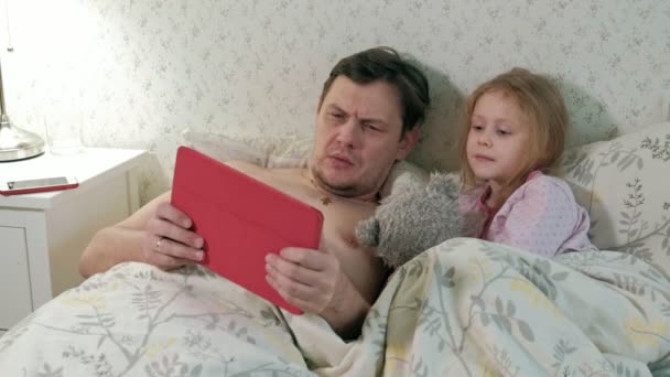Táta a malou dceru na posteli hraje na tabletu — Stock video