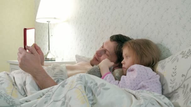 Dad and little daughter on the bed playing on the tablet — Stock Video