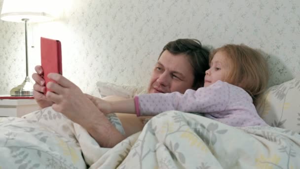 Padre e hija pequeña en la cama jugando en la tableta — Vídeos de Stock