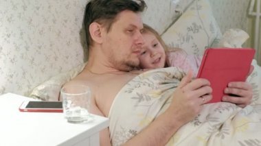 Baba ve küçük kızı tablet üzerinde oynarken yatakta