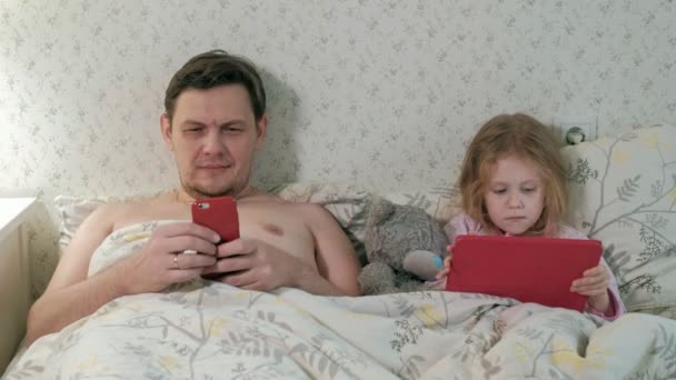 Papa en dochtertje op het bed op de tablet spelen — Stockvideo