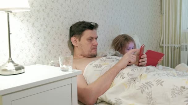 Папа и маленькая дочь на кровати играют на планшете — стоковое видео