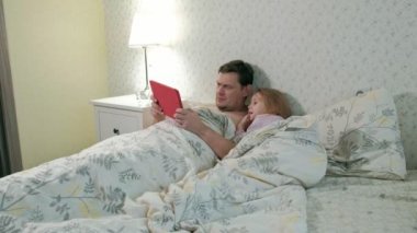 Baba ve küçük kızı tablet üzerinde oynarken yatakta