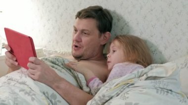 Baba ve küçük kızı tablet üzerinde oynarken yatakta