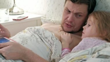 Baba ve küçük kızı tablet üzerinde oynarken yatakta