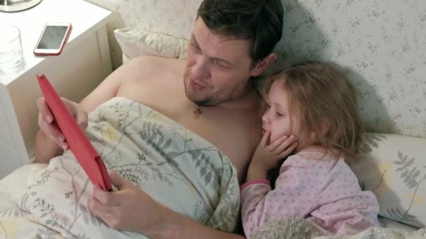 Pappa och lilla dotter på sängen spelar på tabletten — Stockvideo