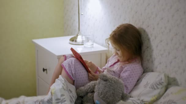 Kleines Mädchen spielt im Bett auf Tablet — Stockvideo