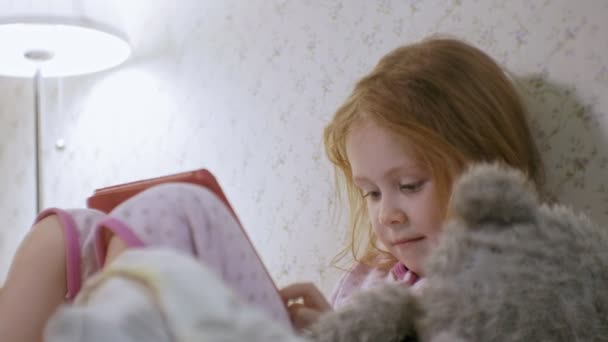 Niña en la cama jugando en la tableta — Vídeos de Stock