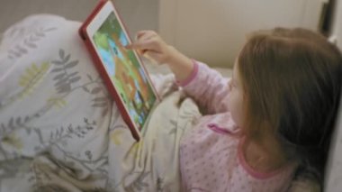 gece yatmadan önce Pembe pijama tablet, gece lambası odasında oynarken yatakta sarışın dağınık saçlı küçük bir kız portre
