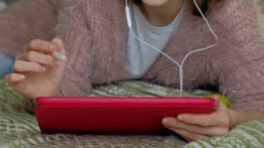 Mutlu kız müzik ve evde yatak odasında bir tablet kullanarak ekran kalemi ile çizer. Web sörf, mesafe çalışma anlayışı, serbest meslek