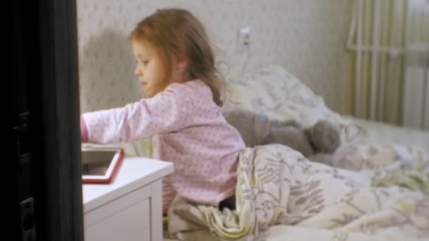 little girl in bed playing on tablet