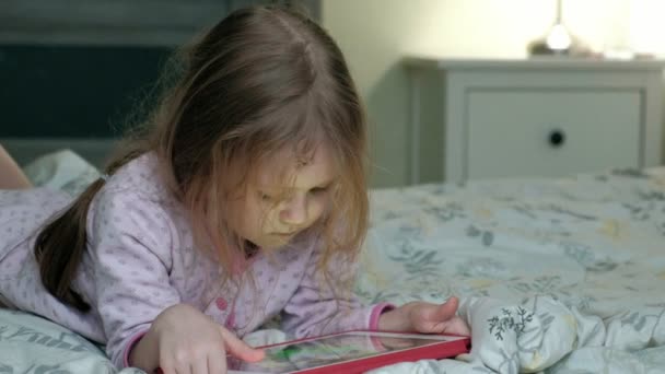 Маленькая девочка в постели играет на планшете — стоковое видео
