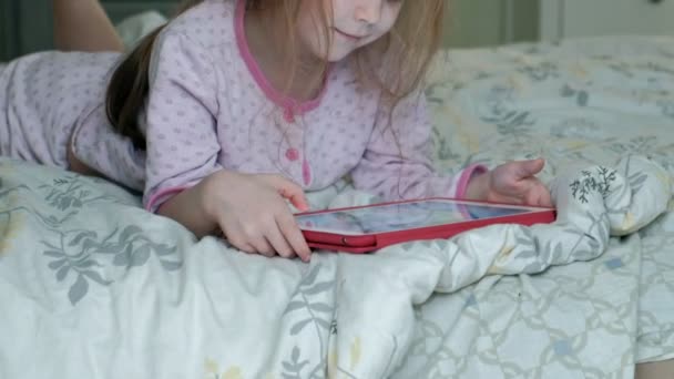 Маленька дівчинка в ліжку грає на планшеті — стокове відео