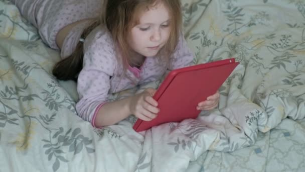 Niña en la cama jugando en la tableta — Vídeos de Stock