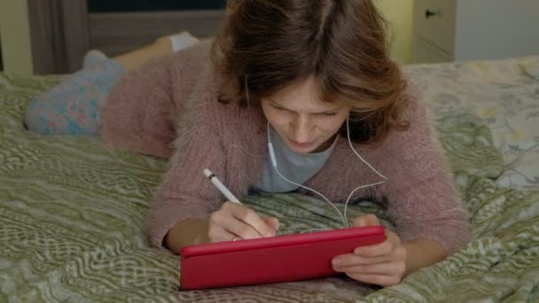 Šťastná dívka poslouchá hudbu a nakreslí pomocí pera tabletu v ložnici doma. Prohlížení webu, vzdálenost pojetí práce, na volné noze — Stock video