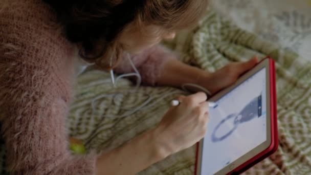 音楽を聴いて幸せな女の子と自宅の寝室でタブレットを使用してスタイラスで描画します。Web サーフィン、距離作業概念、フリーランサー — ストック動画