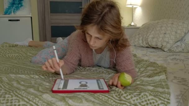 Chica feliz escuchando música y dibuja con un lápiz usando una tableta en el dormitorio en casa. Web surf, concepción del trabajo a distancia, freelancer — Vídeos de Stock