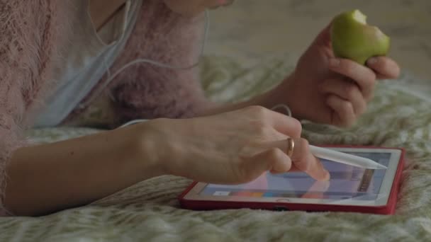 Chica feliz escuchando música y dibuja con un lápiz usando una tableta en el dormitorio en casa. Web surf, concepción del trabajo a distancia, freelancer — Vídeo de stock