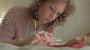 Mutlu kız müzik ve evde yatak odasında bir tablet kullanarak ekran kalemi ile çizer. Web sörf, mesafe çalışma anlayışı, serbest meslek