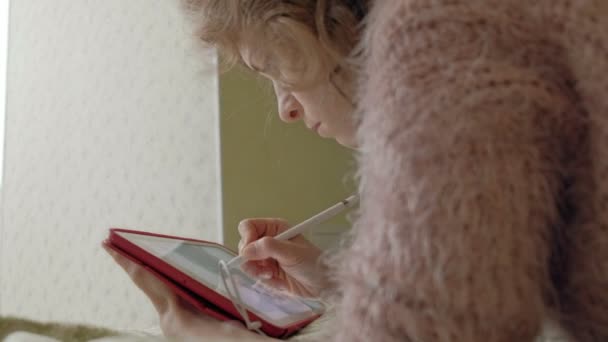 Gelukkig meisje muziek beluisteren en trekt met een stylus met behulp van een tablet in de slaapkamer thuis. Web surfen, afstand werk conceptie, freelancer — Stockvideo