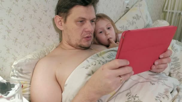 Papa en dochtertje op het bed op de tablet spelen — Stockvideo