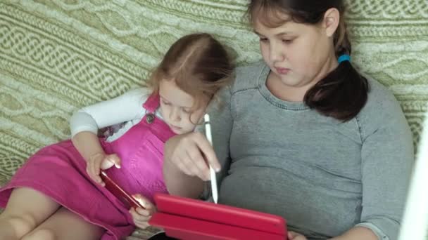 幸せの小さな女の子の姉妹 スタイラスと自宅のソファ 友情の概念 近代的な技術の上に座って電話タブレット コンピューターを使用して友人再生 Web サーフィン — ストック動画