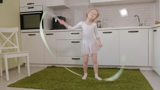 Una bambina felice in costume da bagno bianco da ginnastica, balli con nastro per ginnastica ritmica, salti ed esercizi professionali . — Video Stock